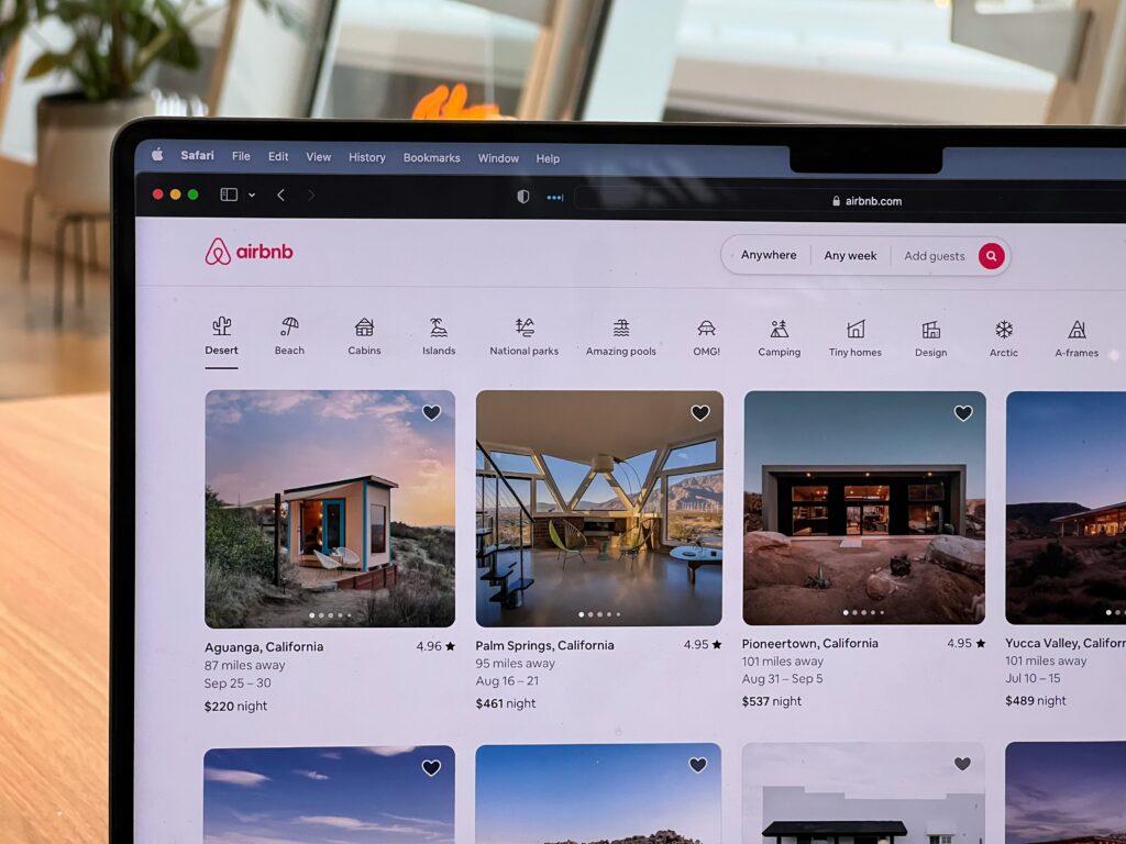 Laptop screen displaying Airbnb listings, highlighting unique accommodation options and amenities as an alternative to hotels.